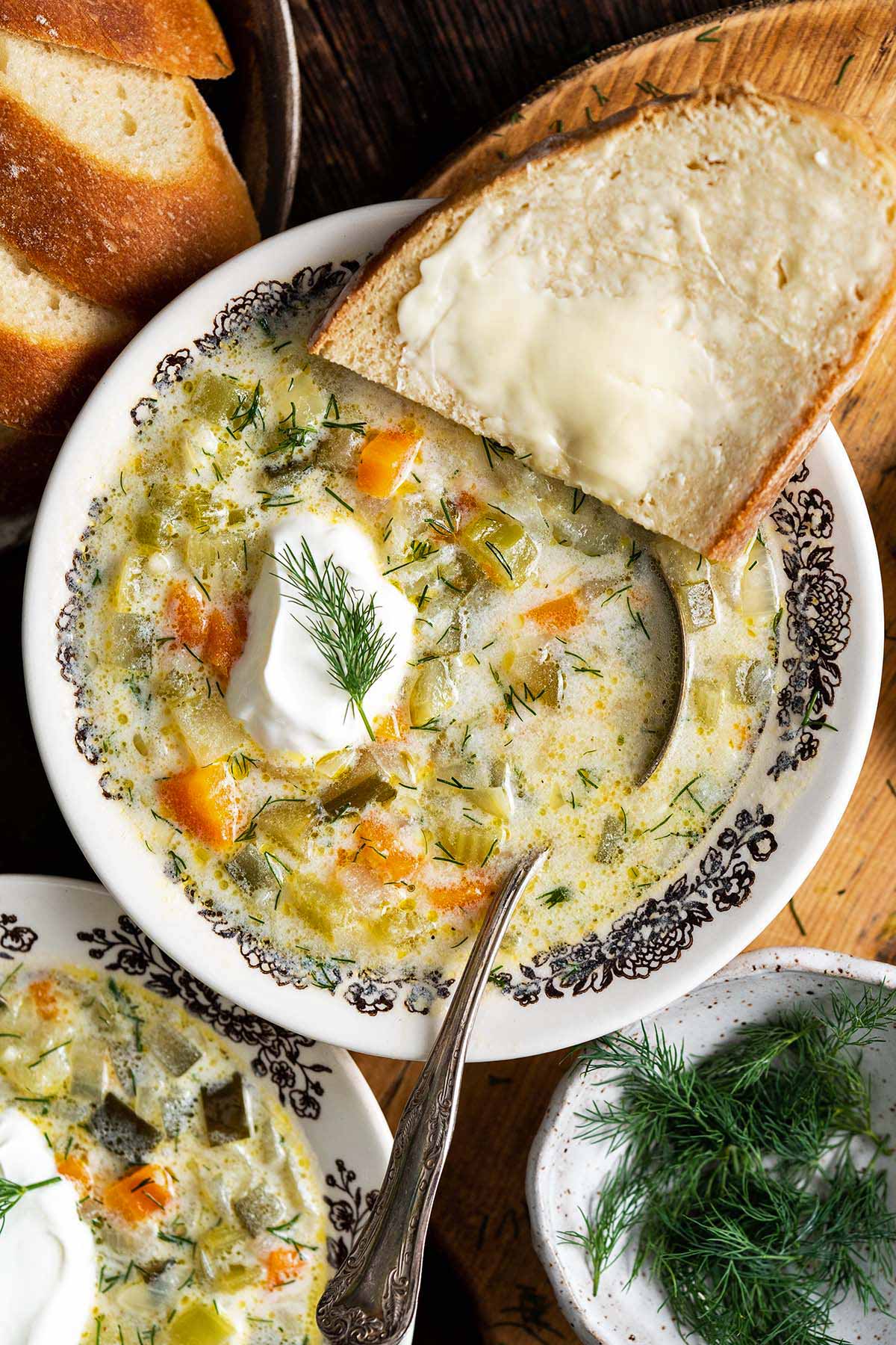 polish dill pickle soup topped with cream cream and a slice of bread on the side