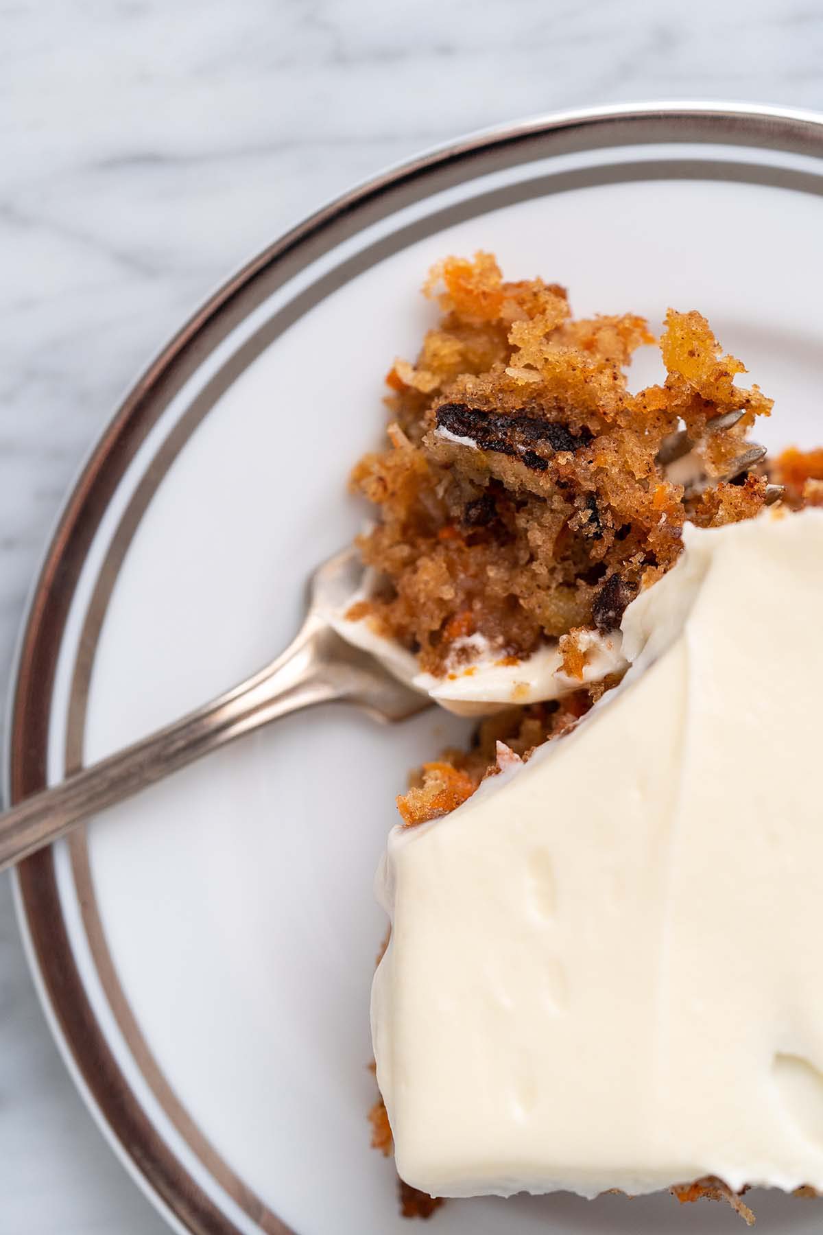 close up top view of silver rimmed plate with a piece of the best moist carrot cake recipe with a bite on a fork