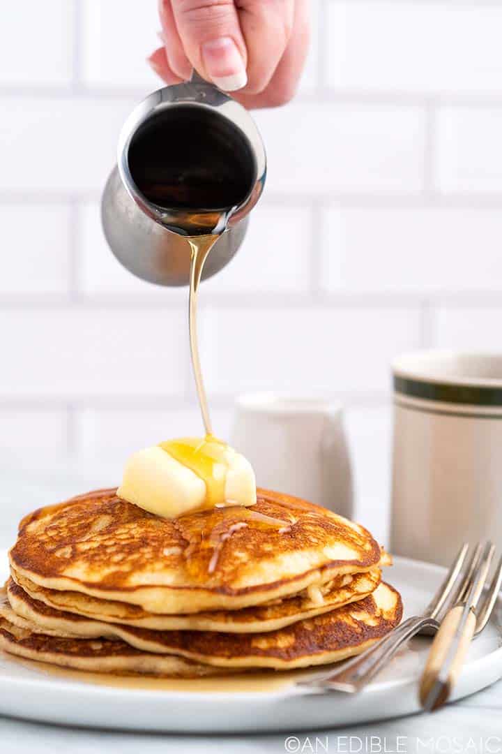 pouring maple syrup on stack of pancakes