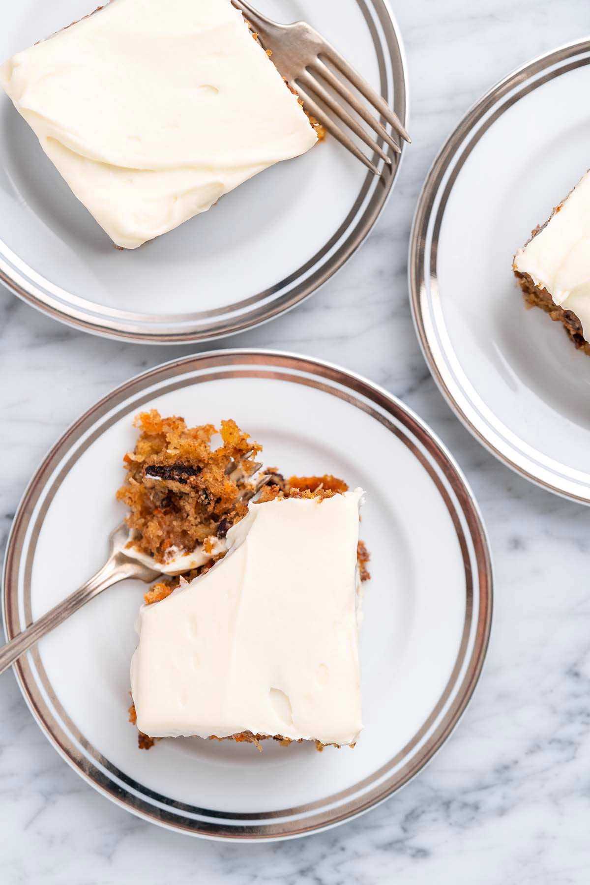 three pieces of carrot cake on dessert plates on marble counter