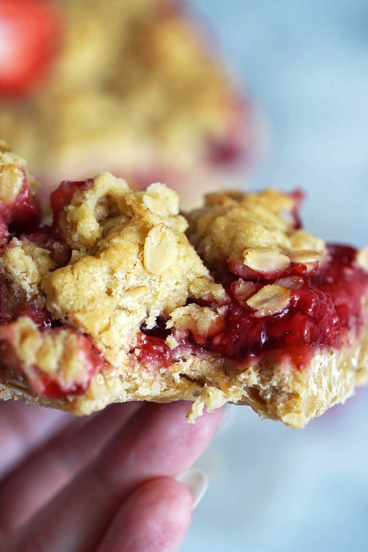 hand holding strawberry oat bar with bite taken to show juicy fruit filling