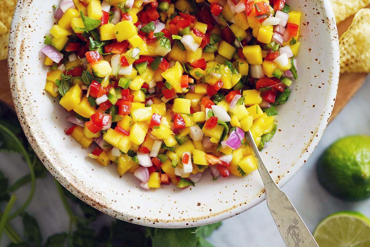 mango salsa in stoneware bowl with cilantro and limes
