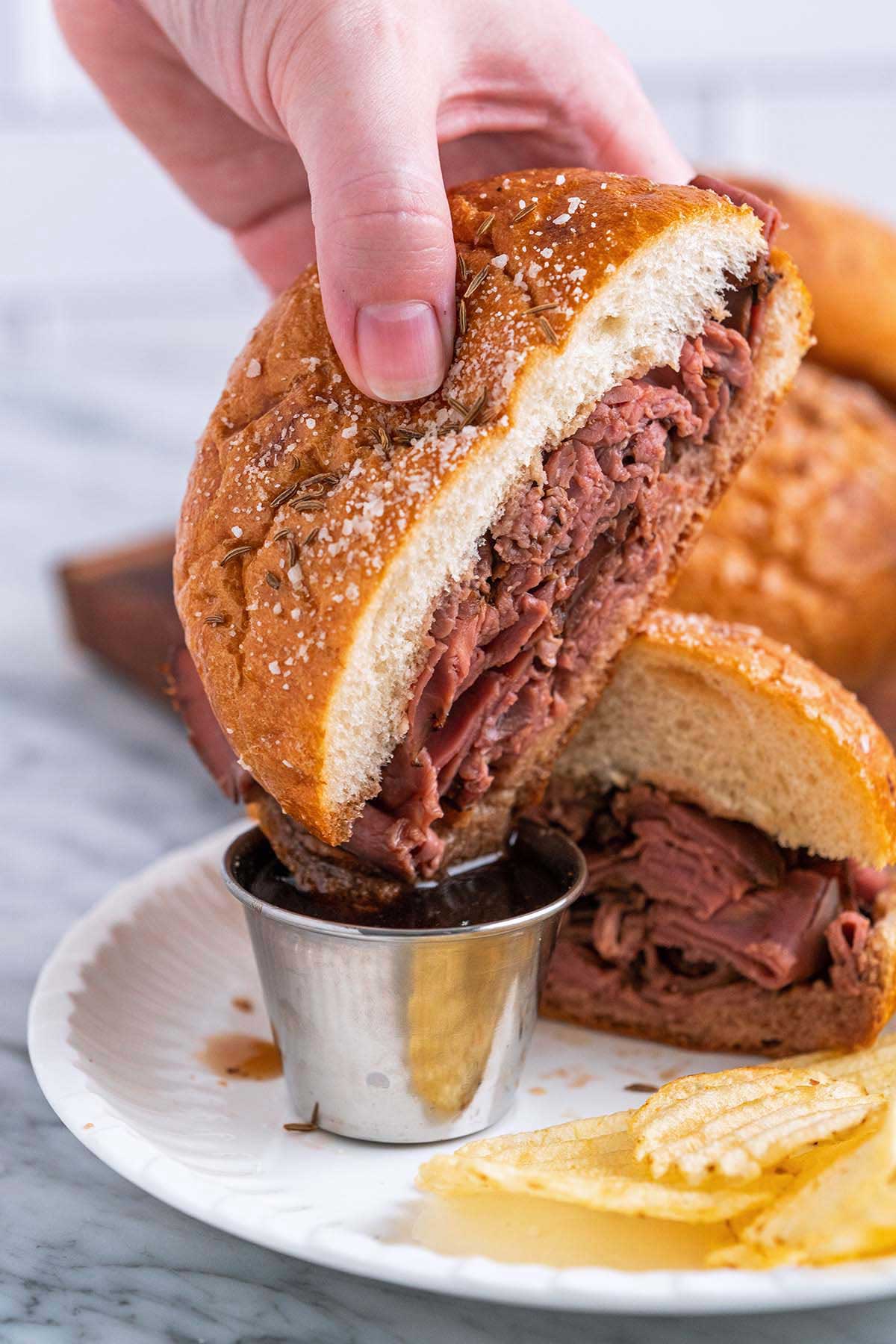 hand dipping roast beef on Weck roll with salt and caraway seeds into au jus