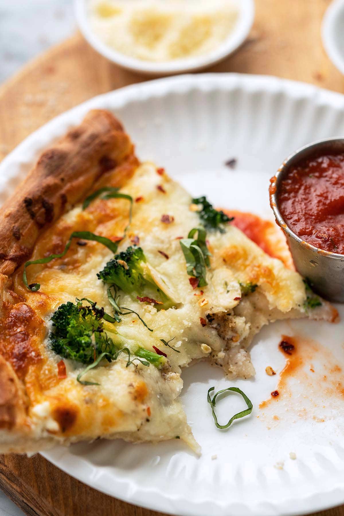 partially eaten slice of Bianca pizza with side of marinara sauce for dipping