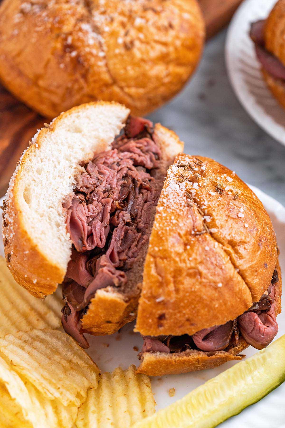 roast beef sandwich on salted caraway seed Kimmelweck roll cut in half to show piles of beef