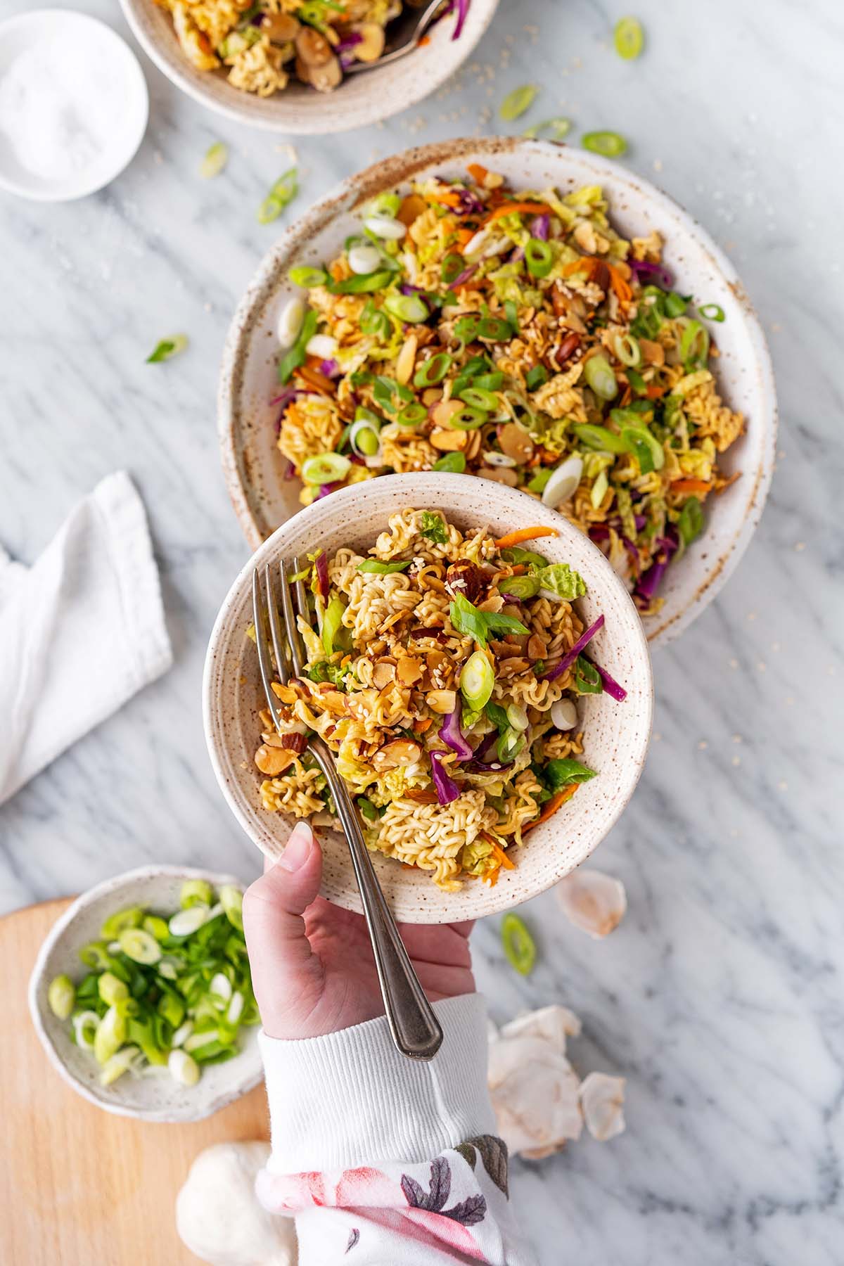 hand holding bowl of crunchy salad using ramen noodles and cabbage