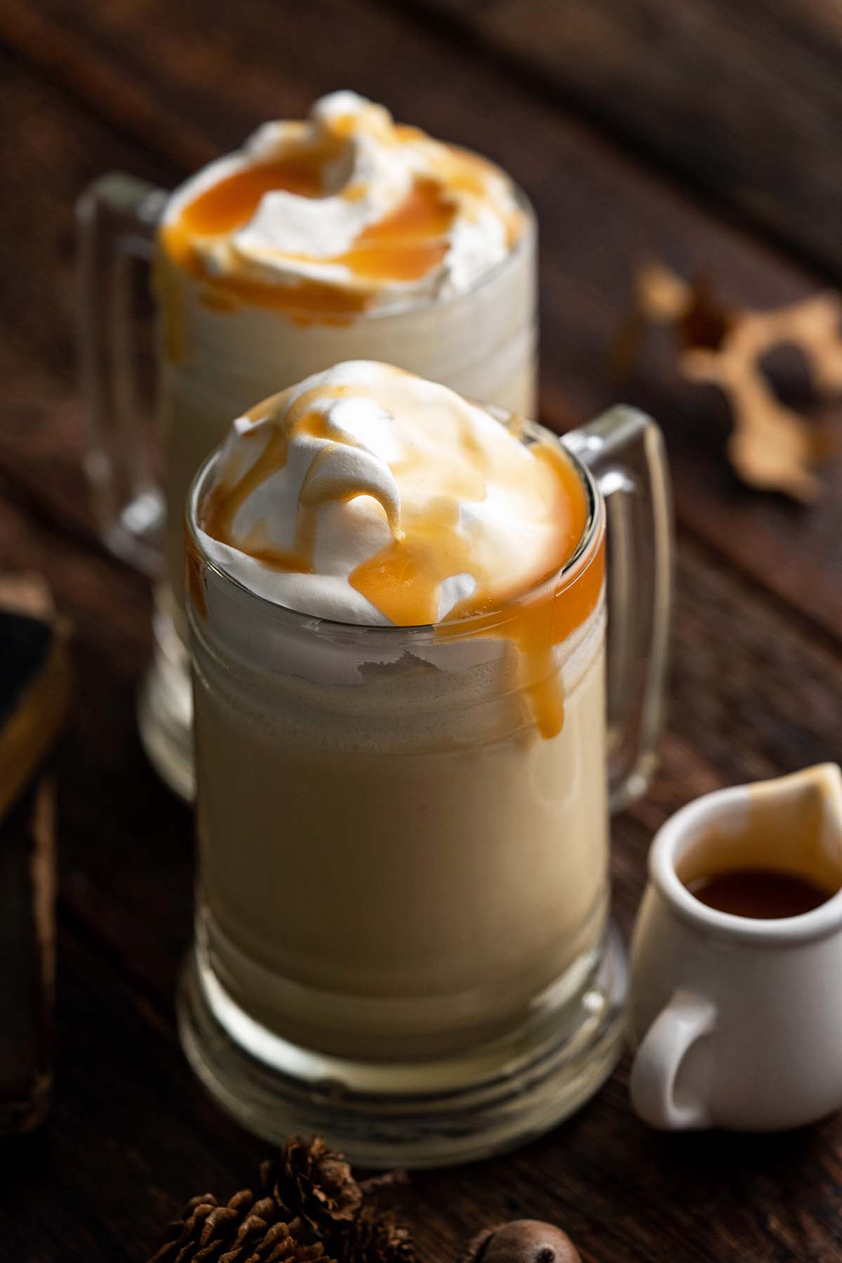 mugs of non alcoholic butterbeer on rustic wooden table with fall leaves and acorns around