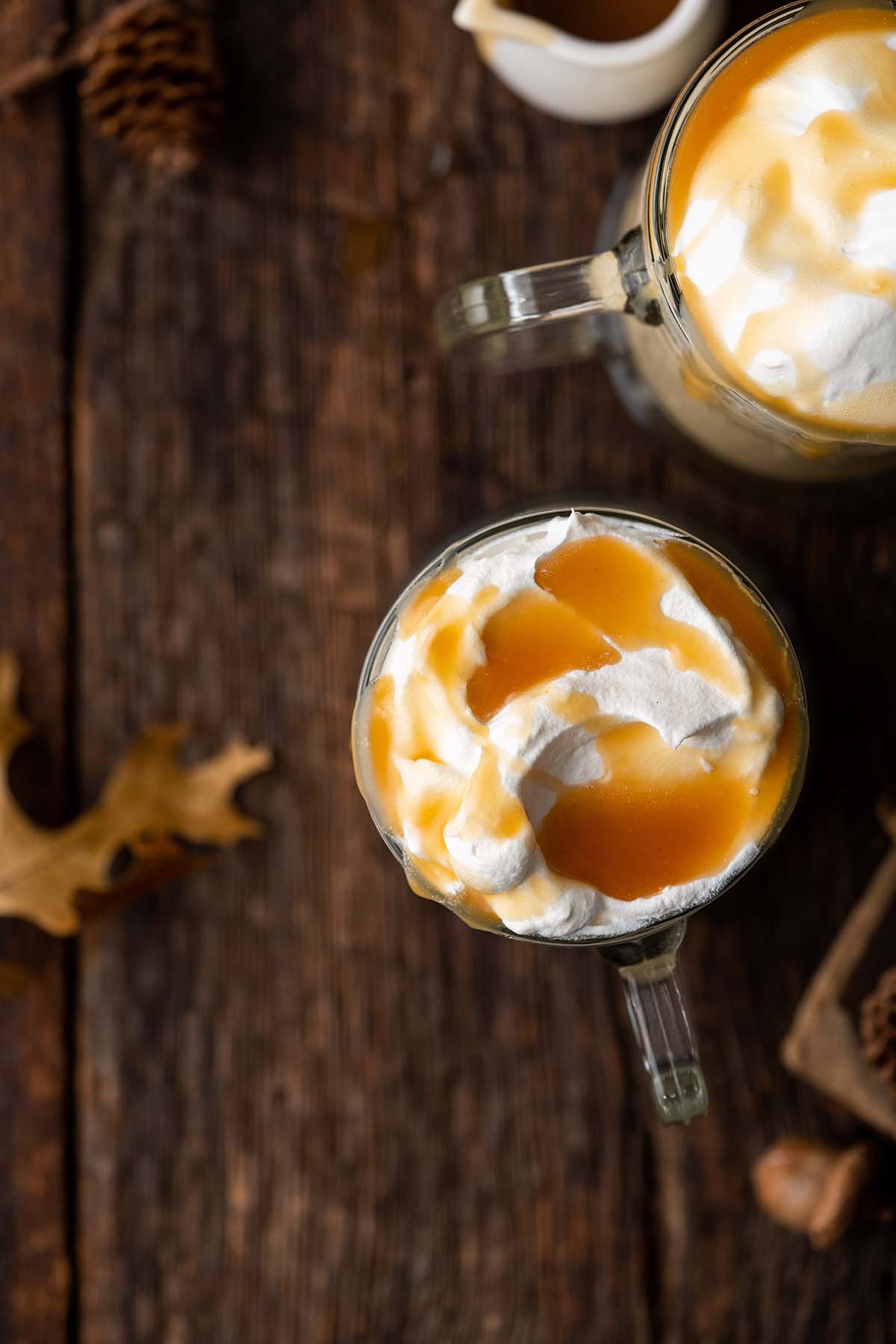 top view of 2 mugs of frozen butterbeer on dark wooden table with butterscotch sauce