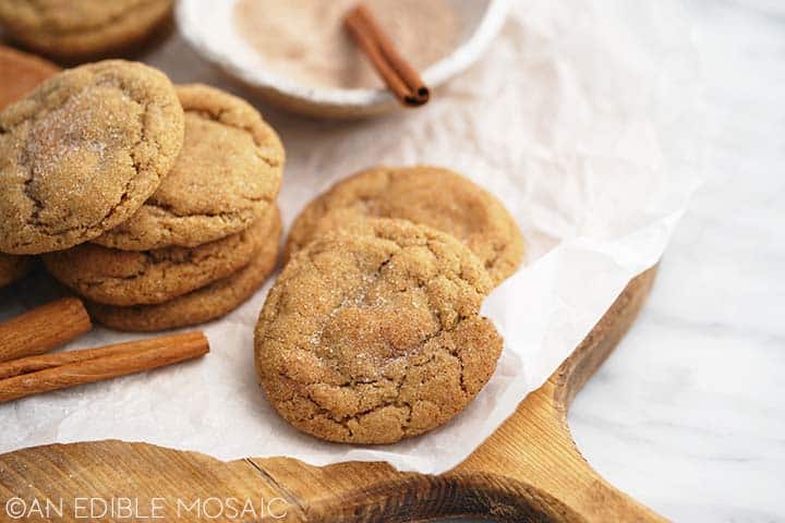 easy apple cinnamon cookies recipe piled on parchment paper on wooden board on marble countertop