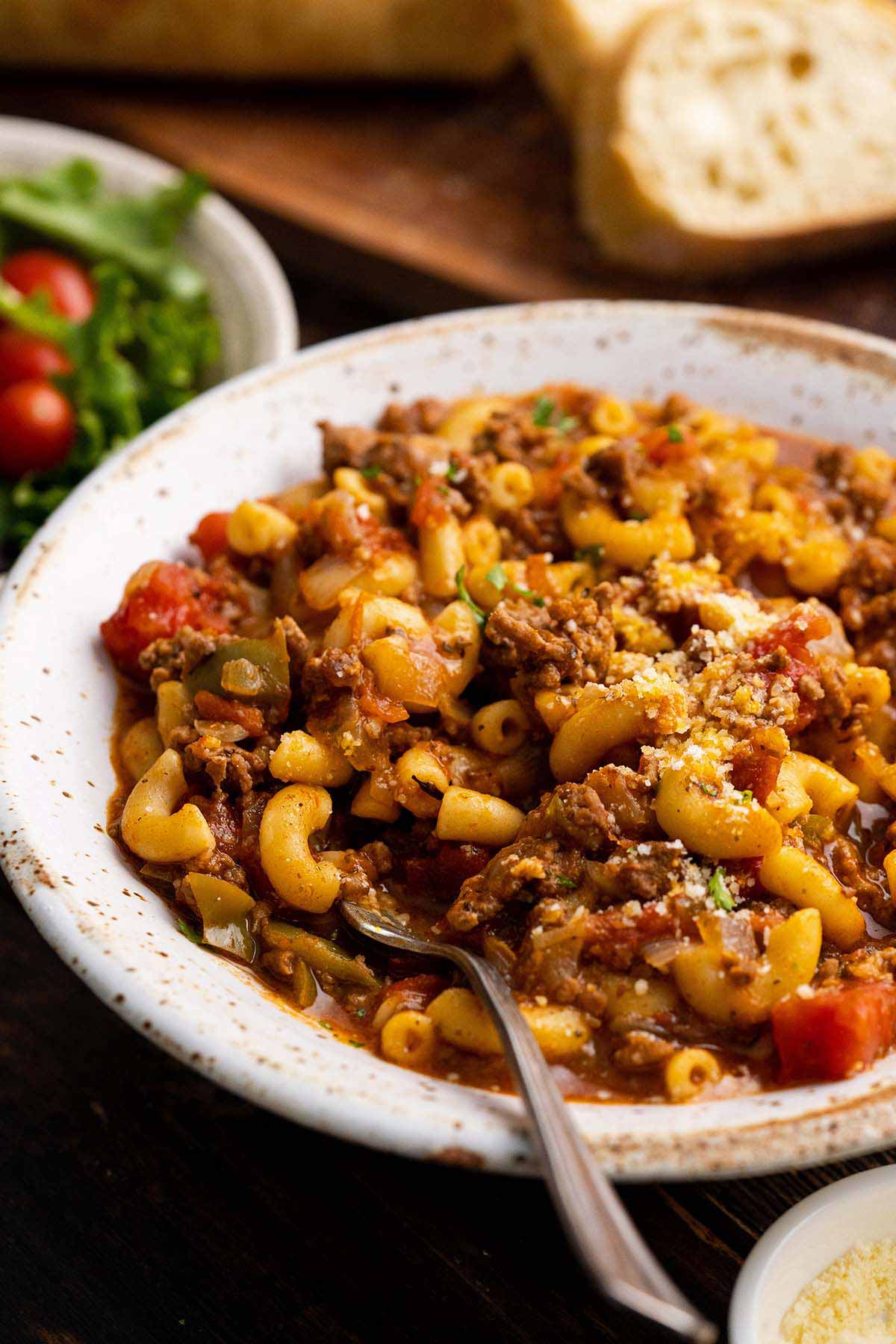 close up front view of easy ground beef goulash with salad and bread