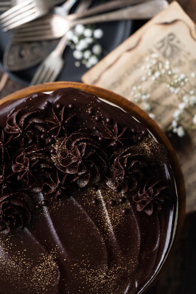 close up top view of birds milk dessert decorated with chocolate ganache roses and edible gold glitter