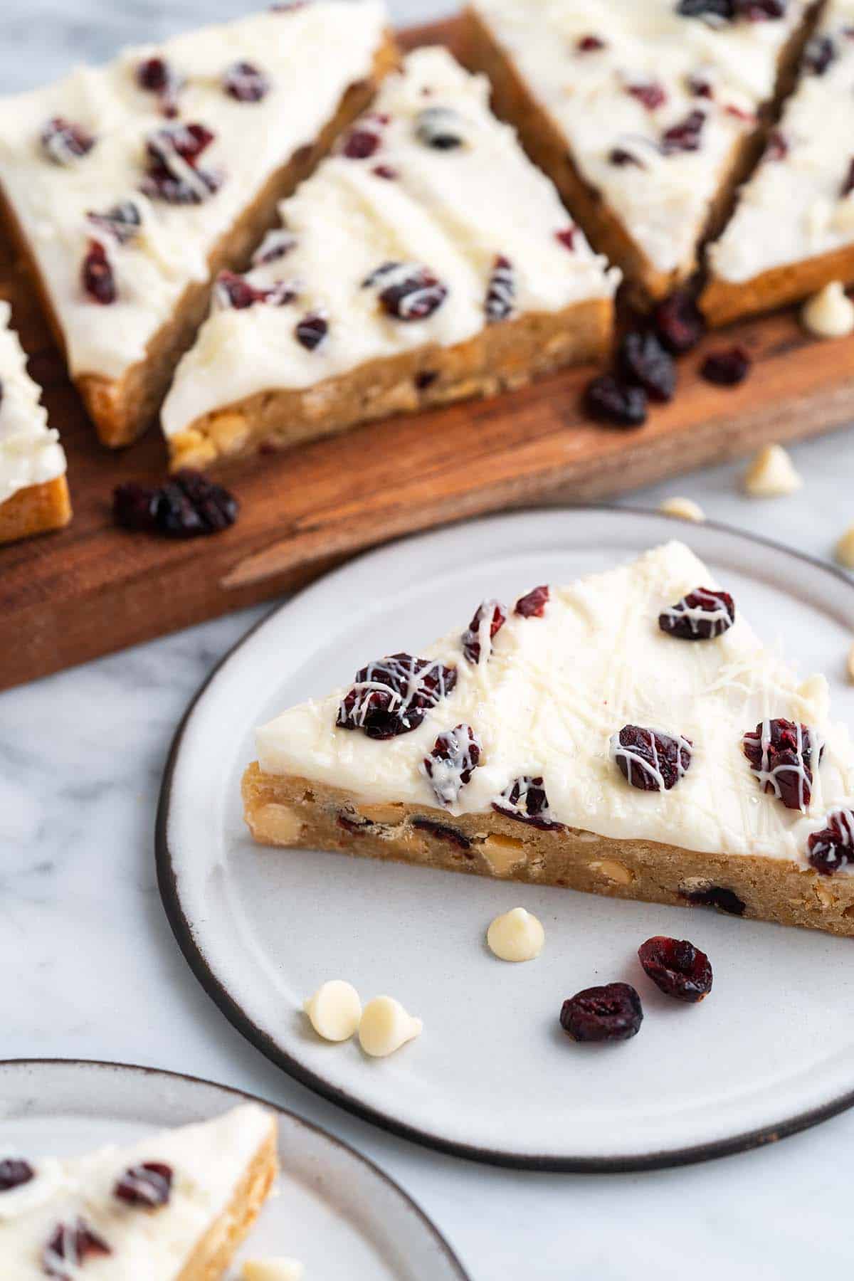 cranberry bliss bar on white ceramic plate with more bars on wooden board in background