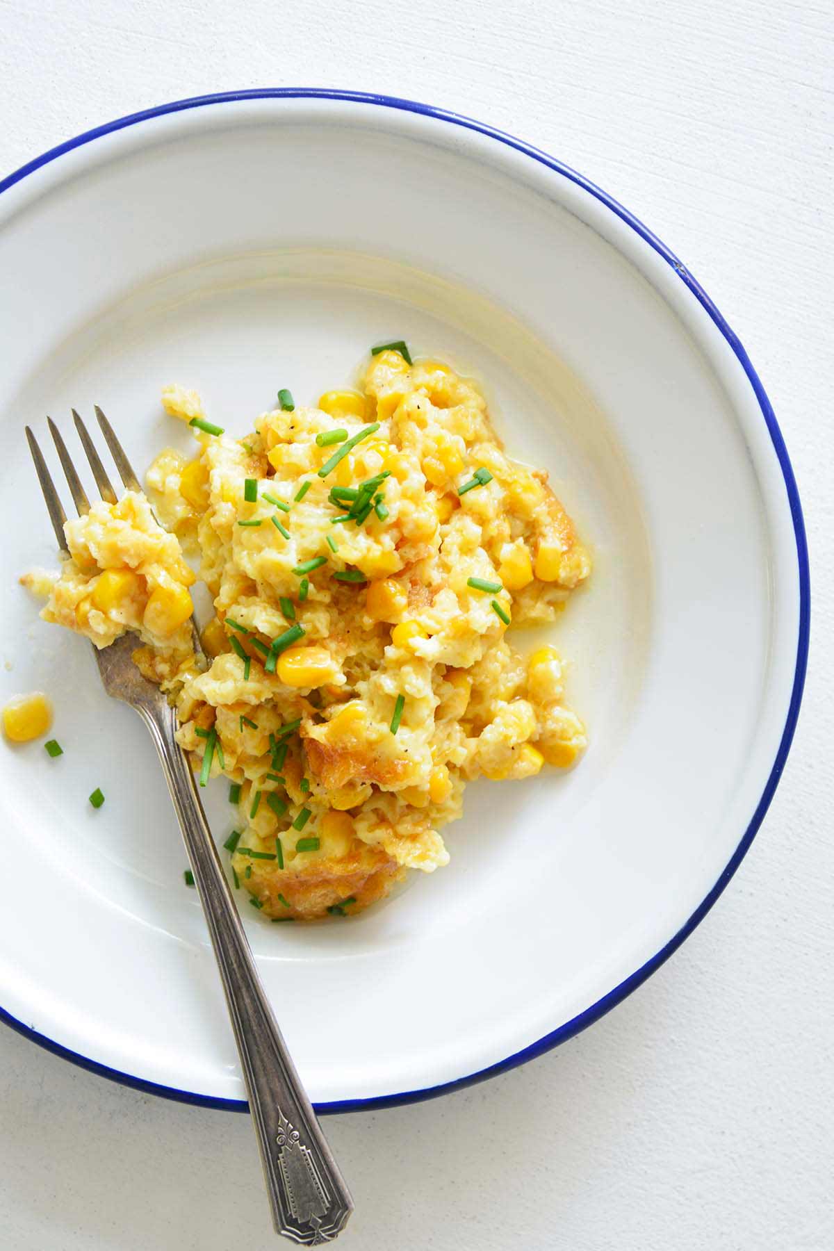 serving of old fashioned creamy corn pudding on white plate with blue rim