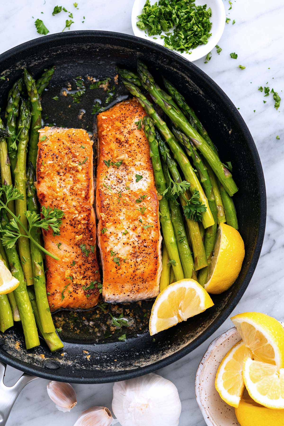 top view of salmon and asparagus with lemon garlic butter in pan on marble countertop