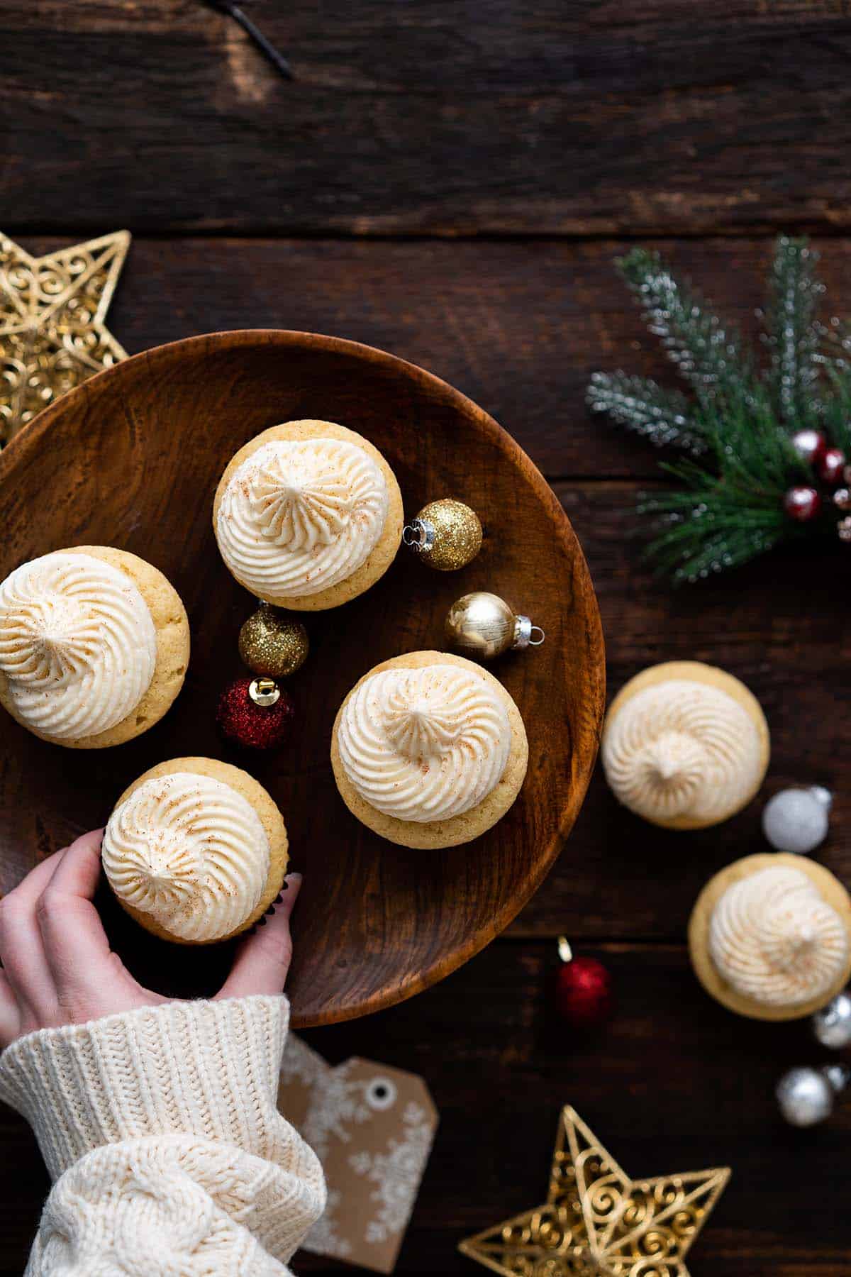 hand reaching in to grab eggnog cupcake off wooden platter