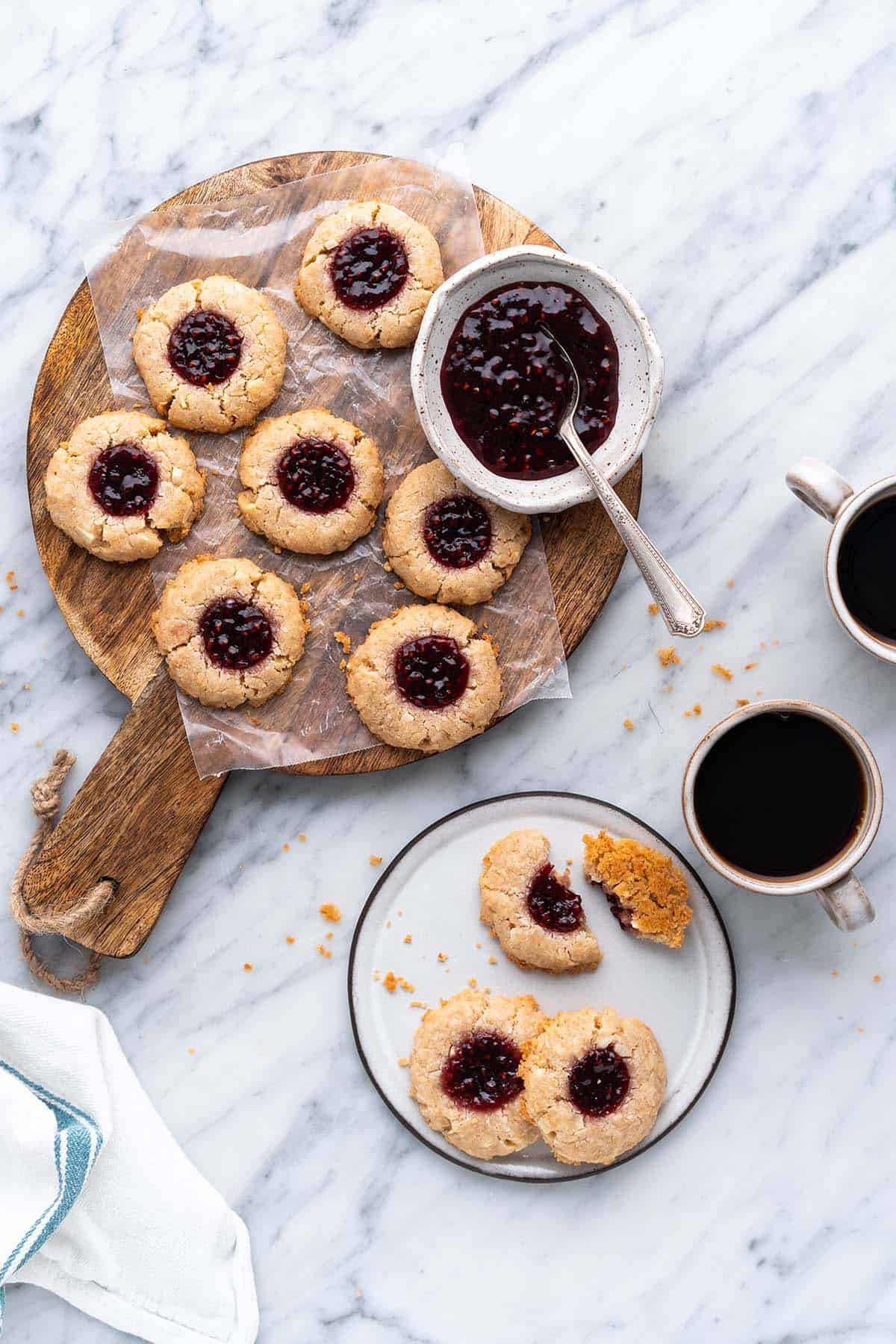 overhead view of jam thumbprint cookies on wooden board on top of marble countertop