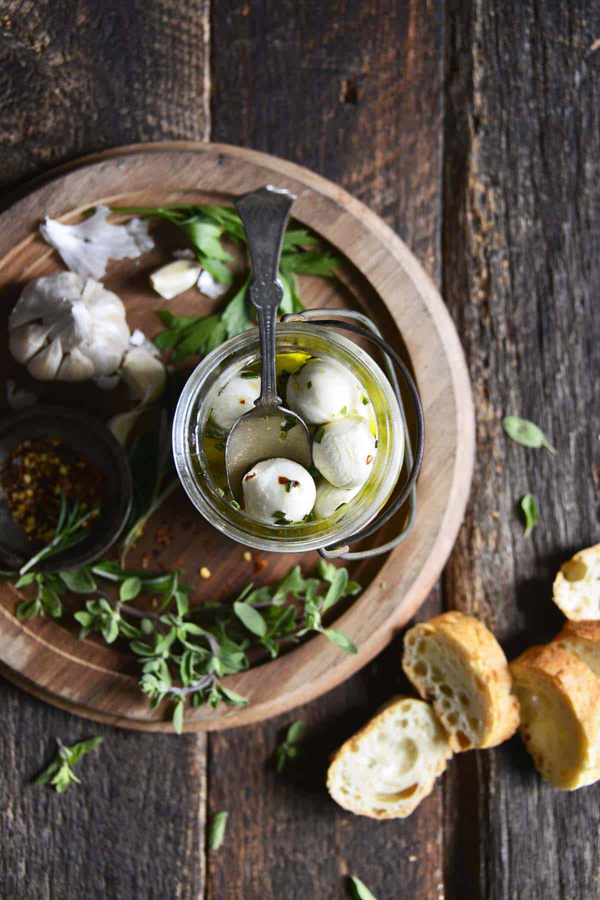 overhead view of olive oil marinated mozzarella balls in glass jar on wooden table