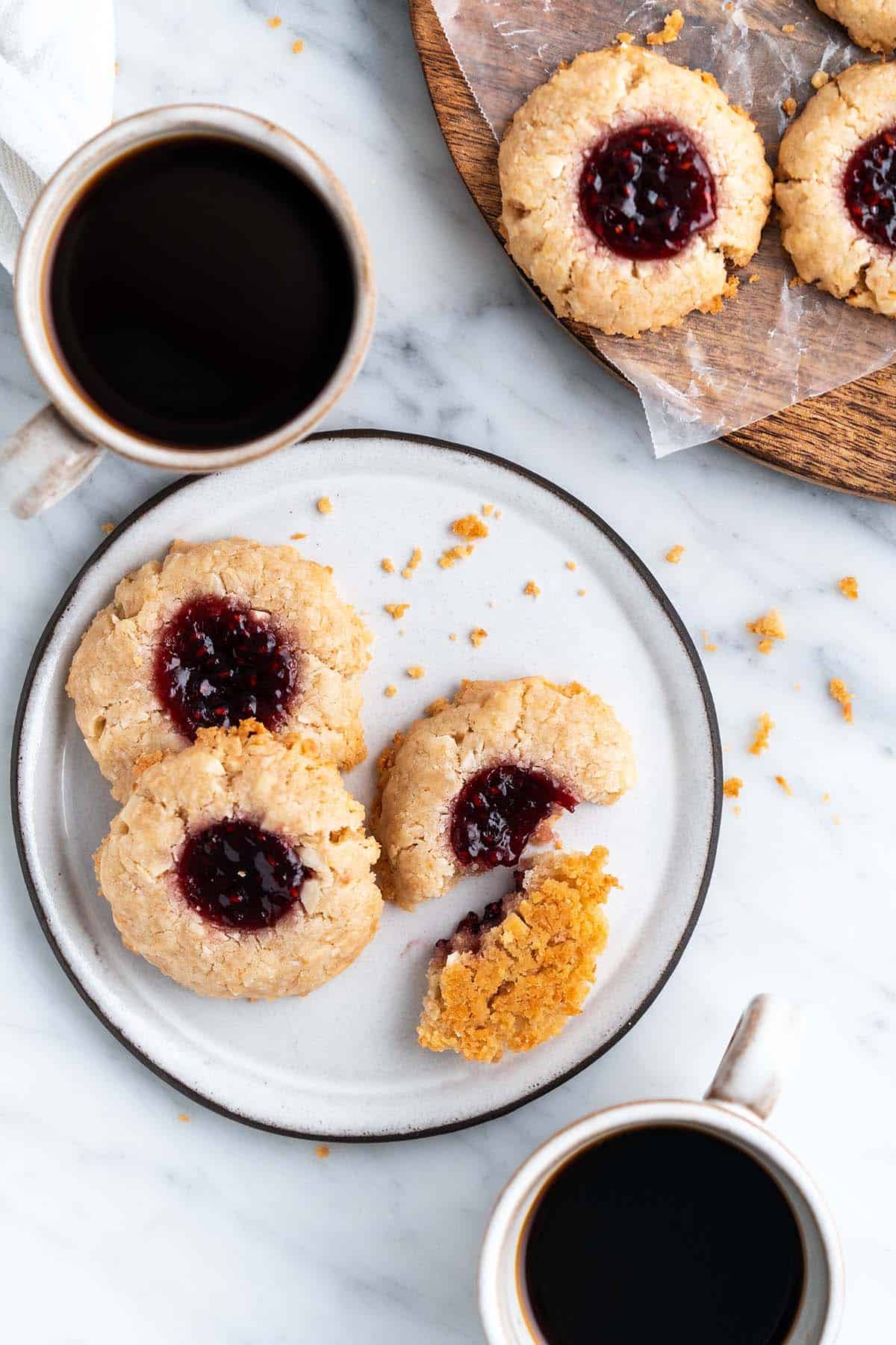plate of vegan jam thumbprint cookies with cups of coffee on side