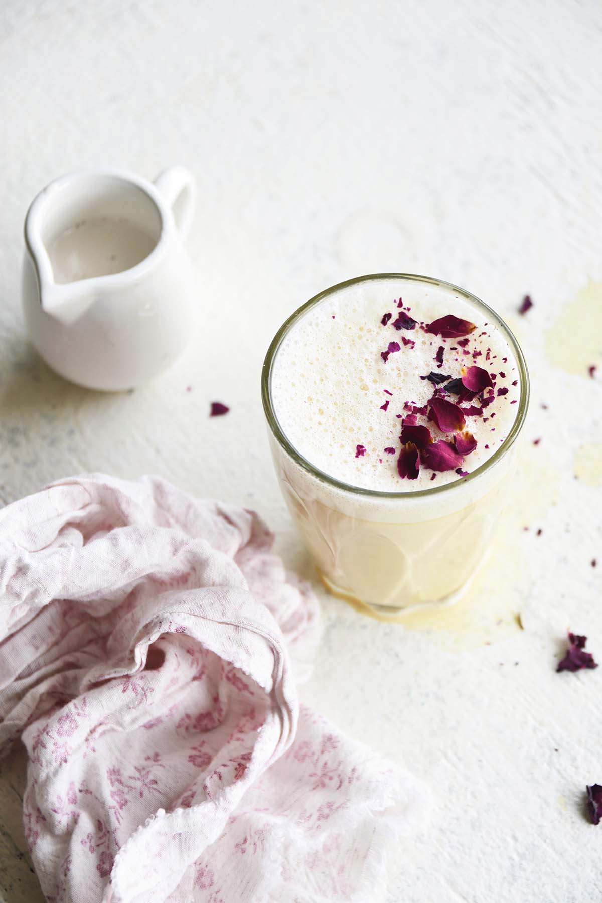 rose latte in glass with small jug of milk