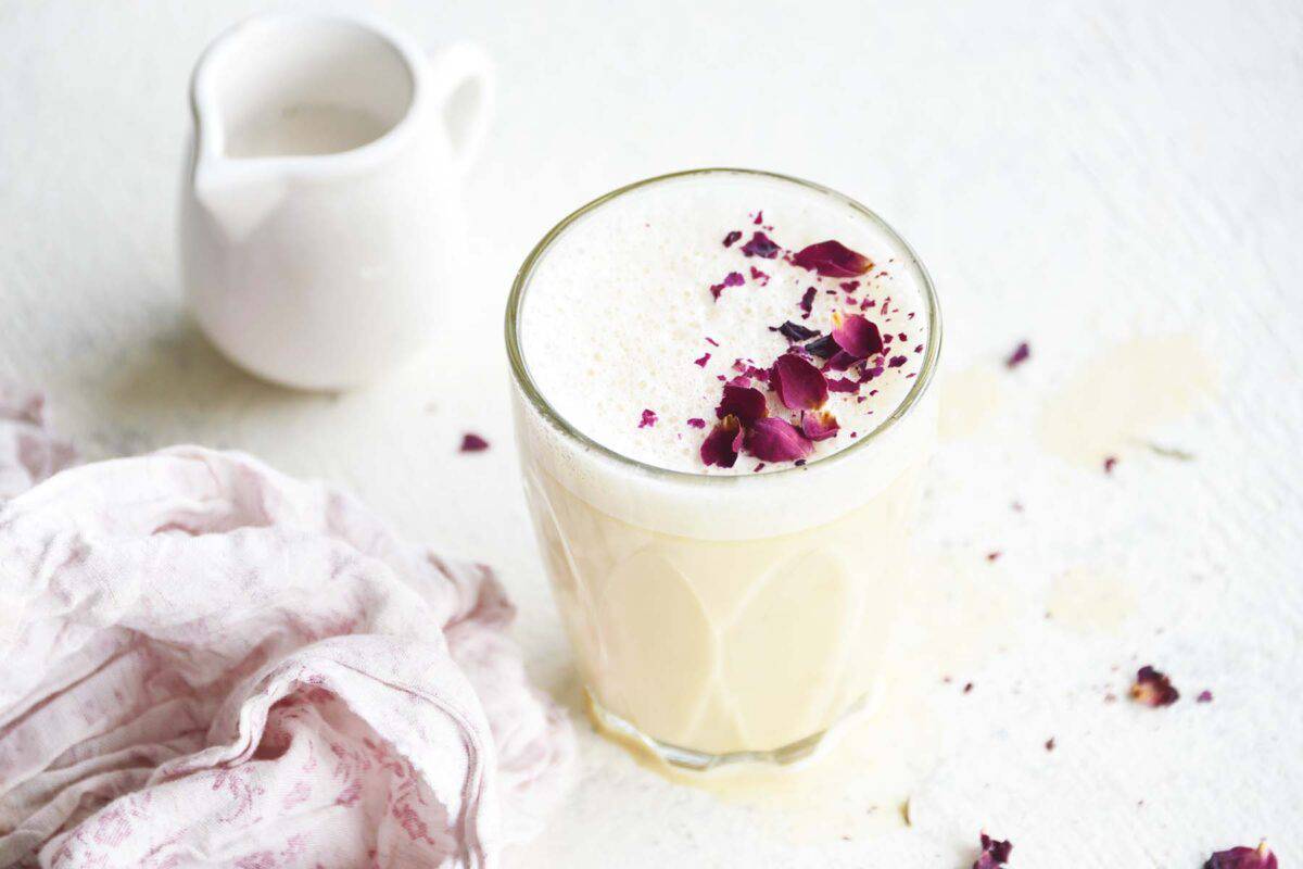 rose milk latte in small glass with dried rose petals on top