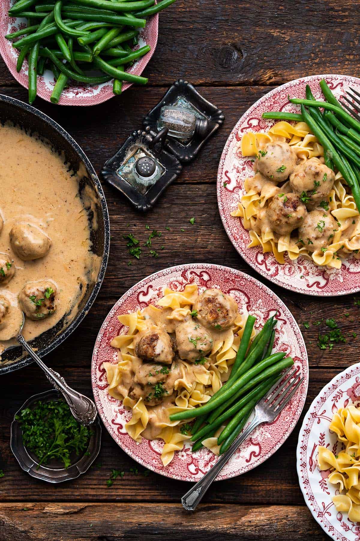 spread of swedish meatball meal with egg noodles and green beans on wooden table