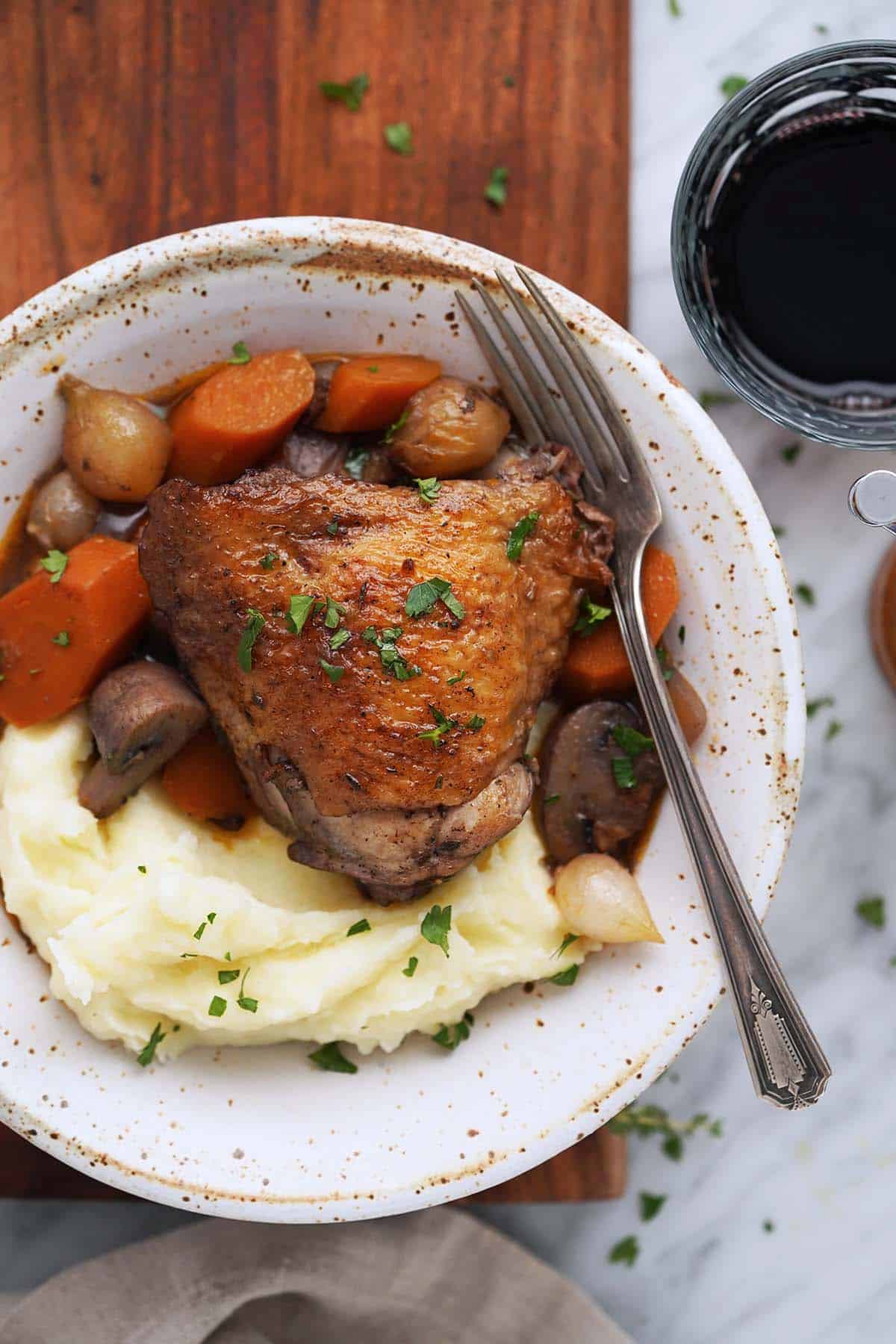 coq au vin in bowl with glass of wine on side