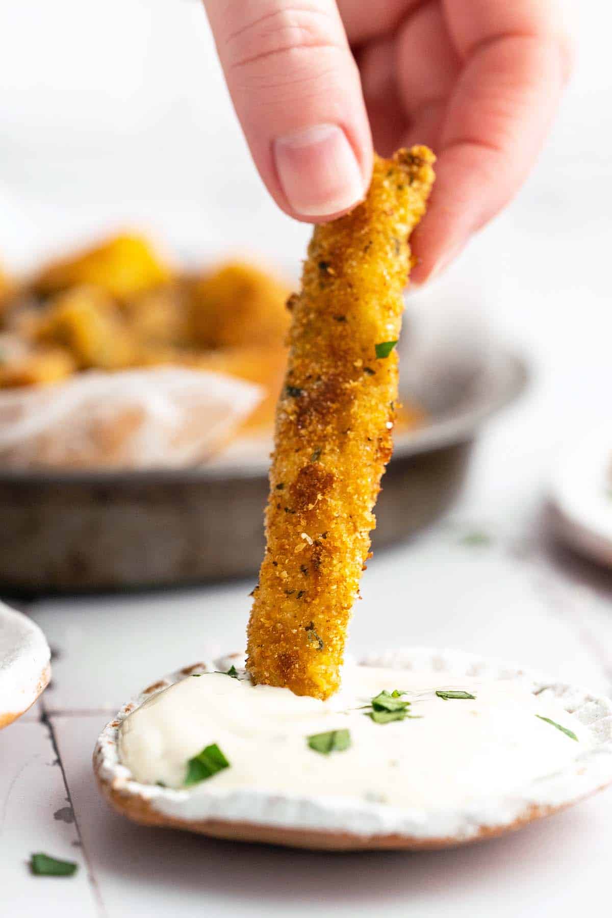 hand dipping zucchini fry into ranch
