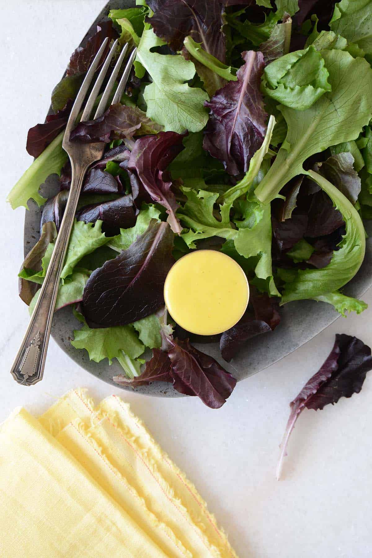 salad greens on platter with small dish of mango salad dressing