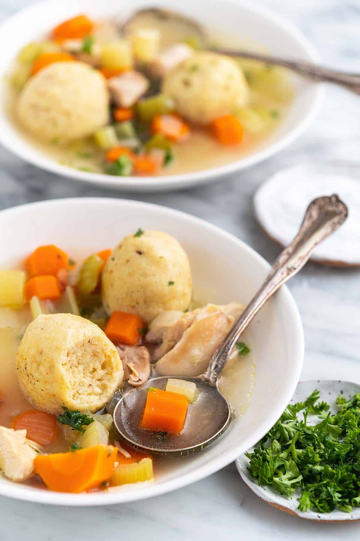 front view of bowls of chicken matzo balls soup with bite taken out of one ball to show fluffy texture