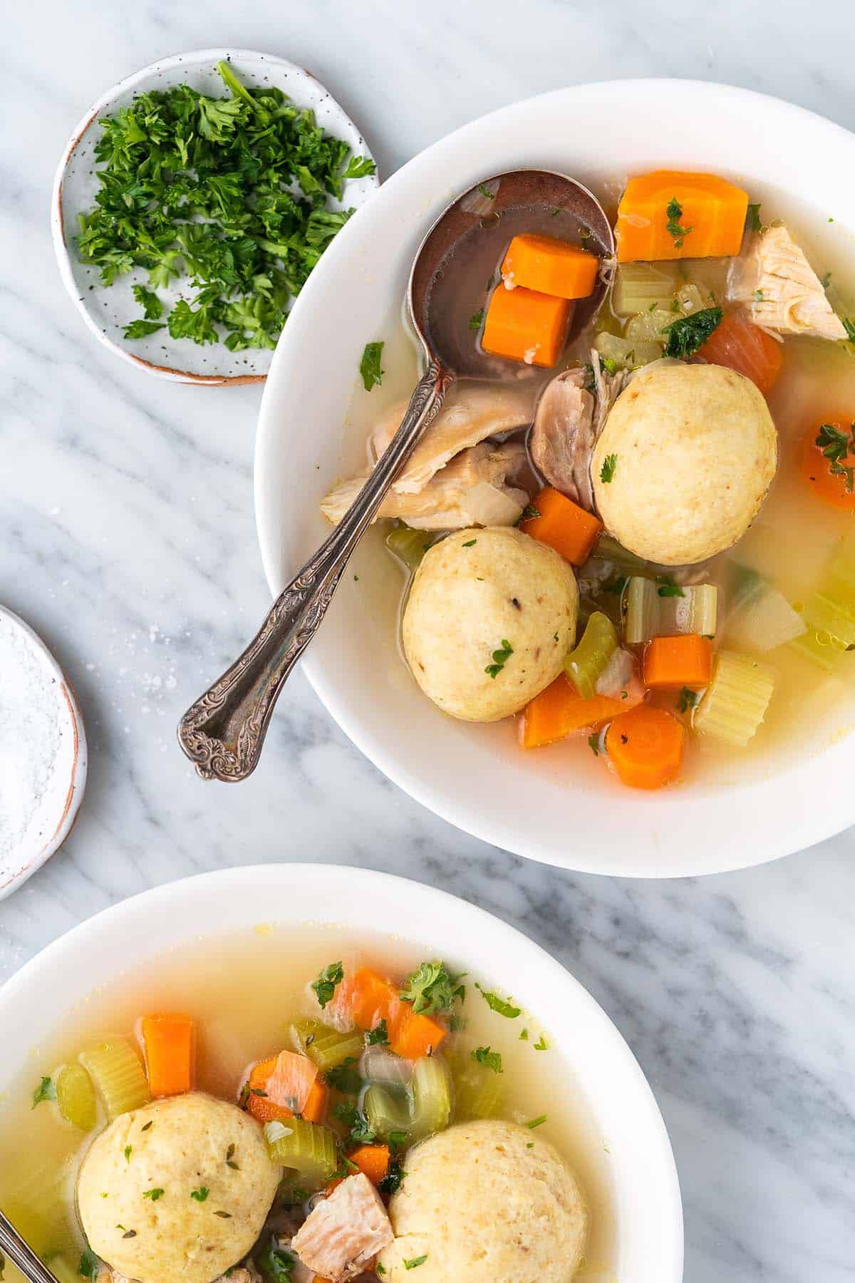 overhead view of bowls of chicken matzo ball soup on marble countertop