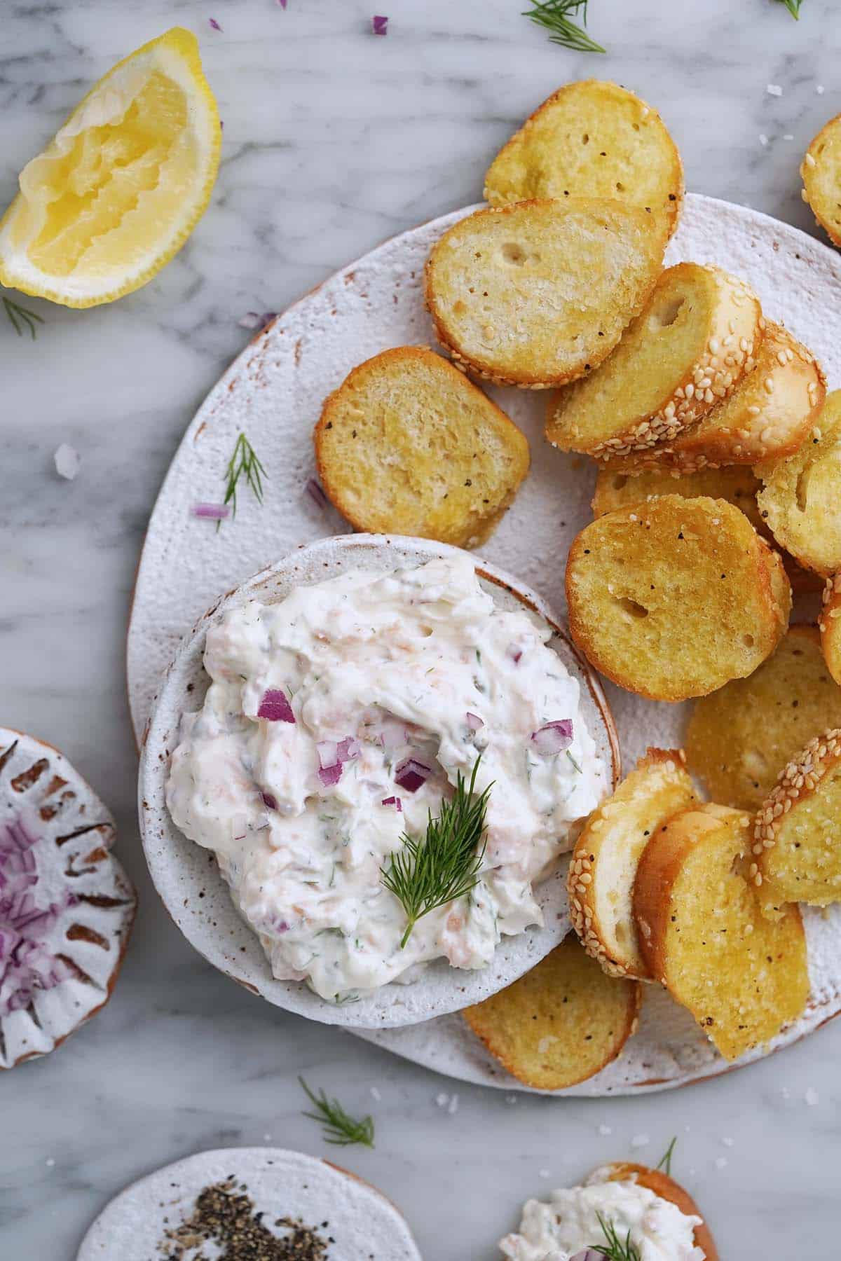 top view of smoked salmon dip and bagel chips on rustic white plate on marble countertop