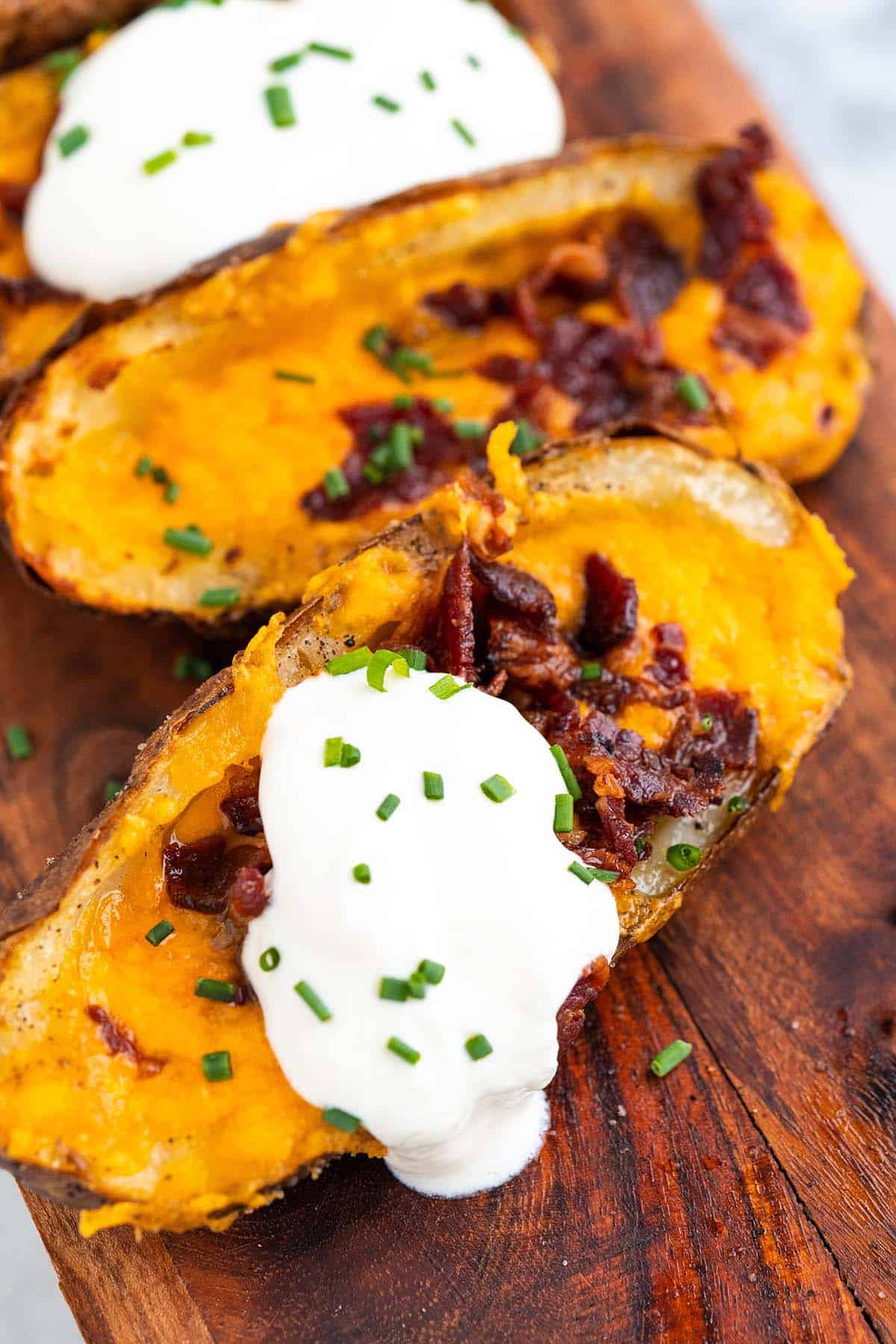 close up of loaded cheesy potato skins on wooden serving platter with sour cream