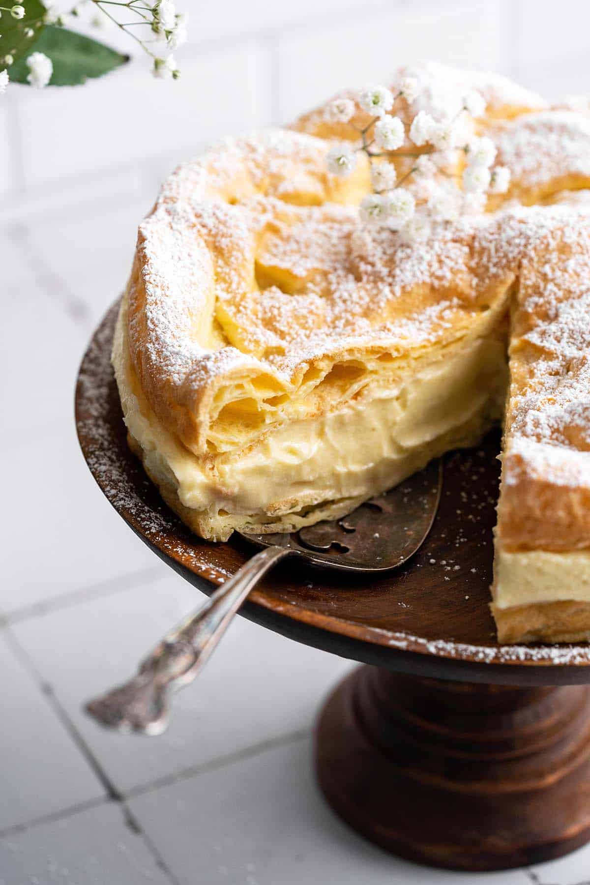 polish karpatka cake with one slice missing on wooden cake stand