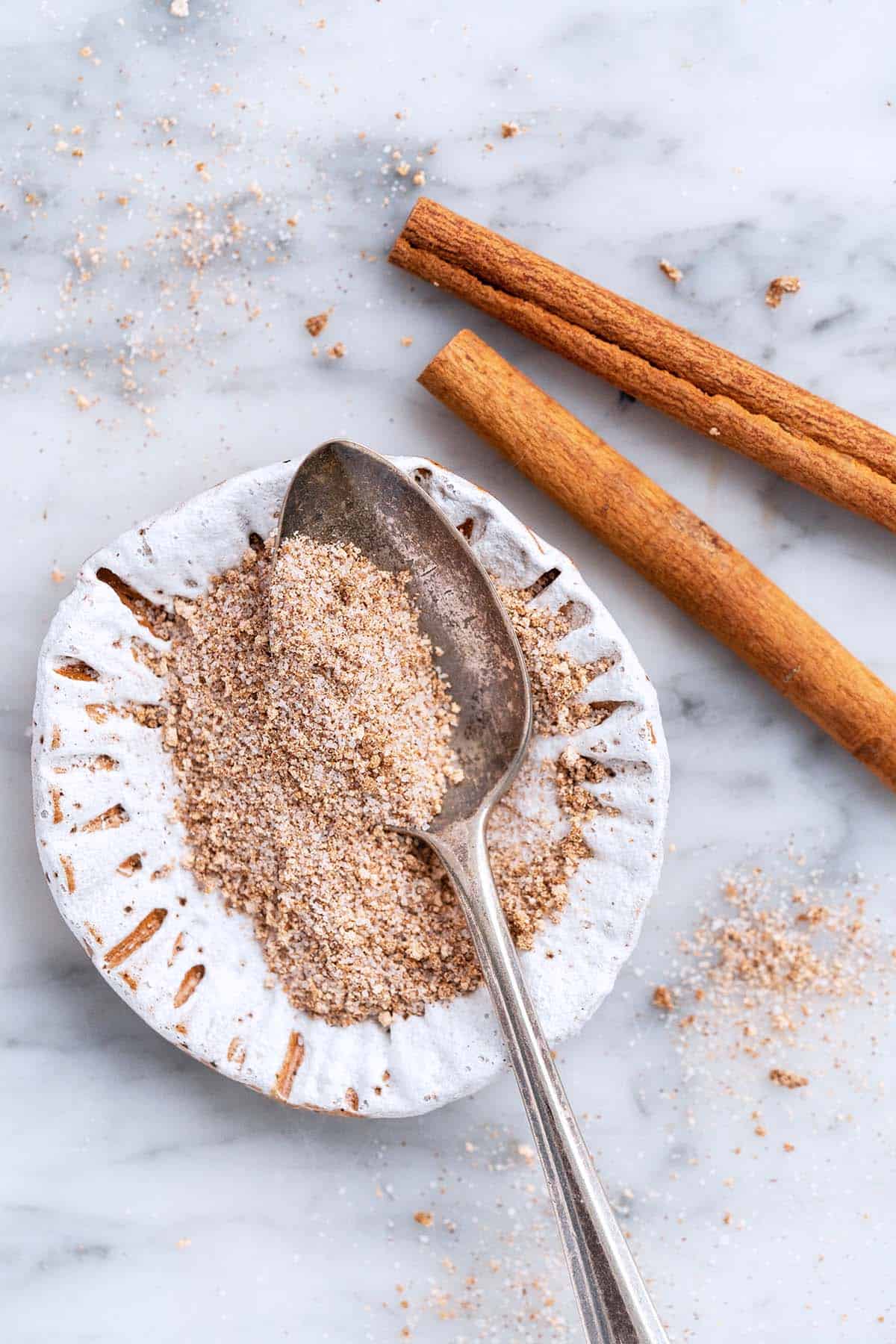 small dish of cinnamon dolce sprinkles topping with vintage spoon on marble countertop