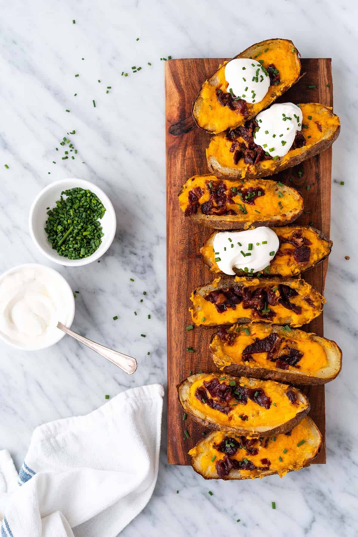 top view of loaded cheesy air fryer potato skins on platter with dishes of sour cream and chives