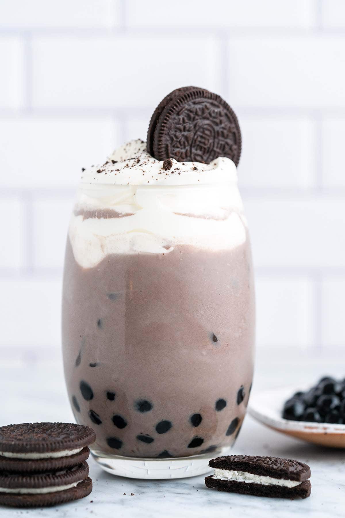front view of oreo boba in glass topped with whipped cream and oreo cookie