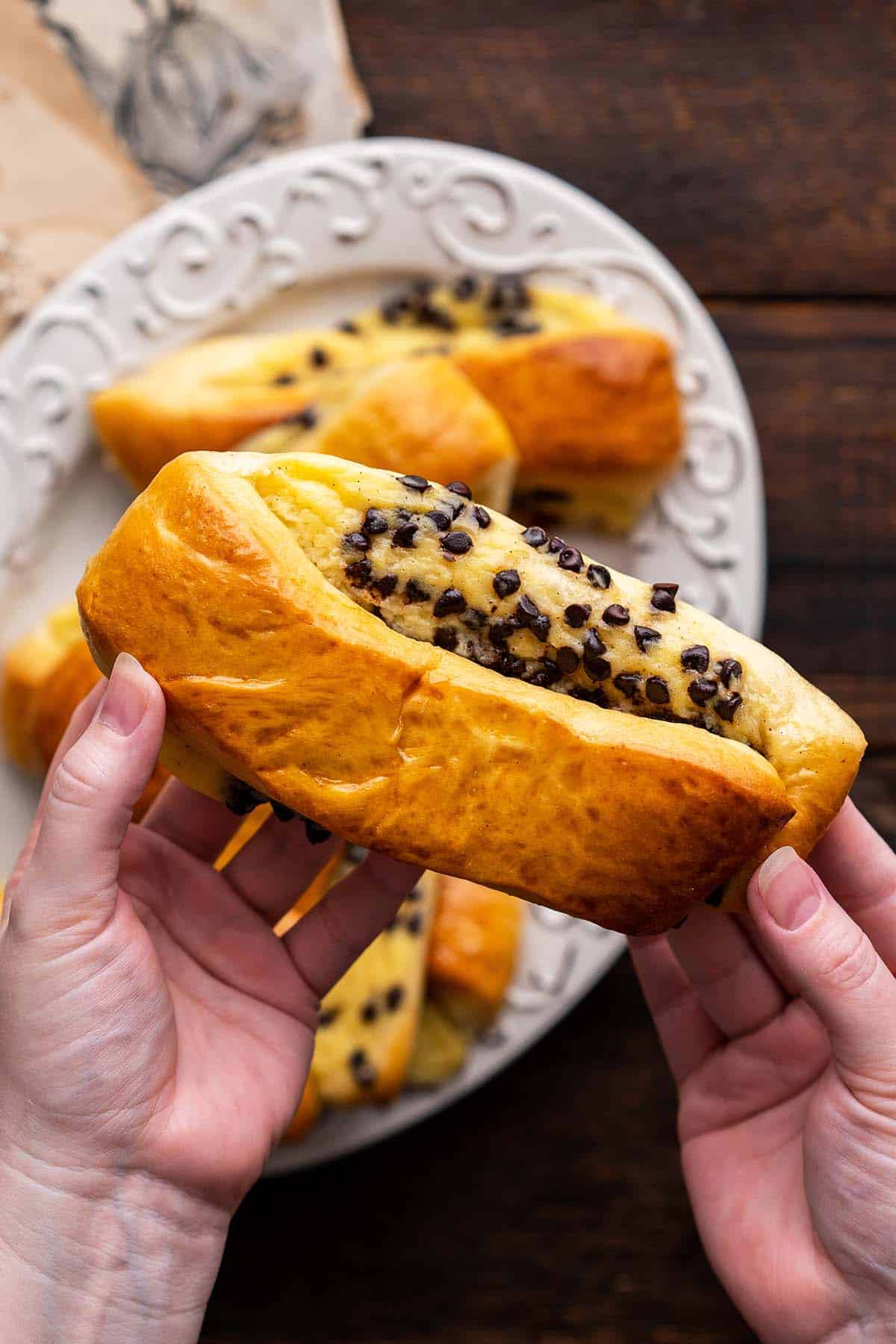 hands holding pain suisse pastry over platter of pastries