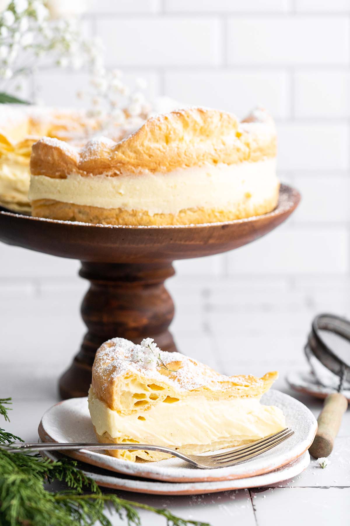 single slice of polish karpatka cake with whole cake on wooden cake stand in background
