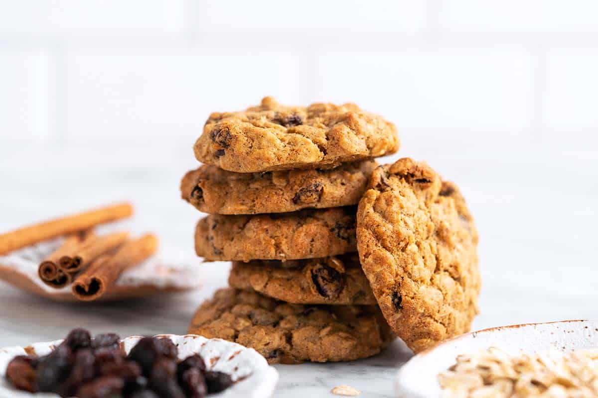 stack of oatmeal raisin cookies with oats raisins and cinnamon sticks on marble countertop