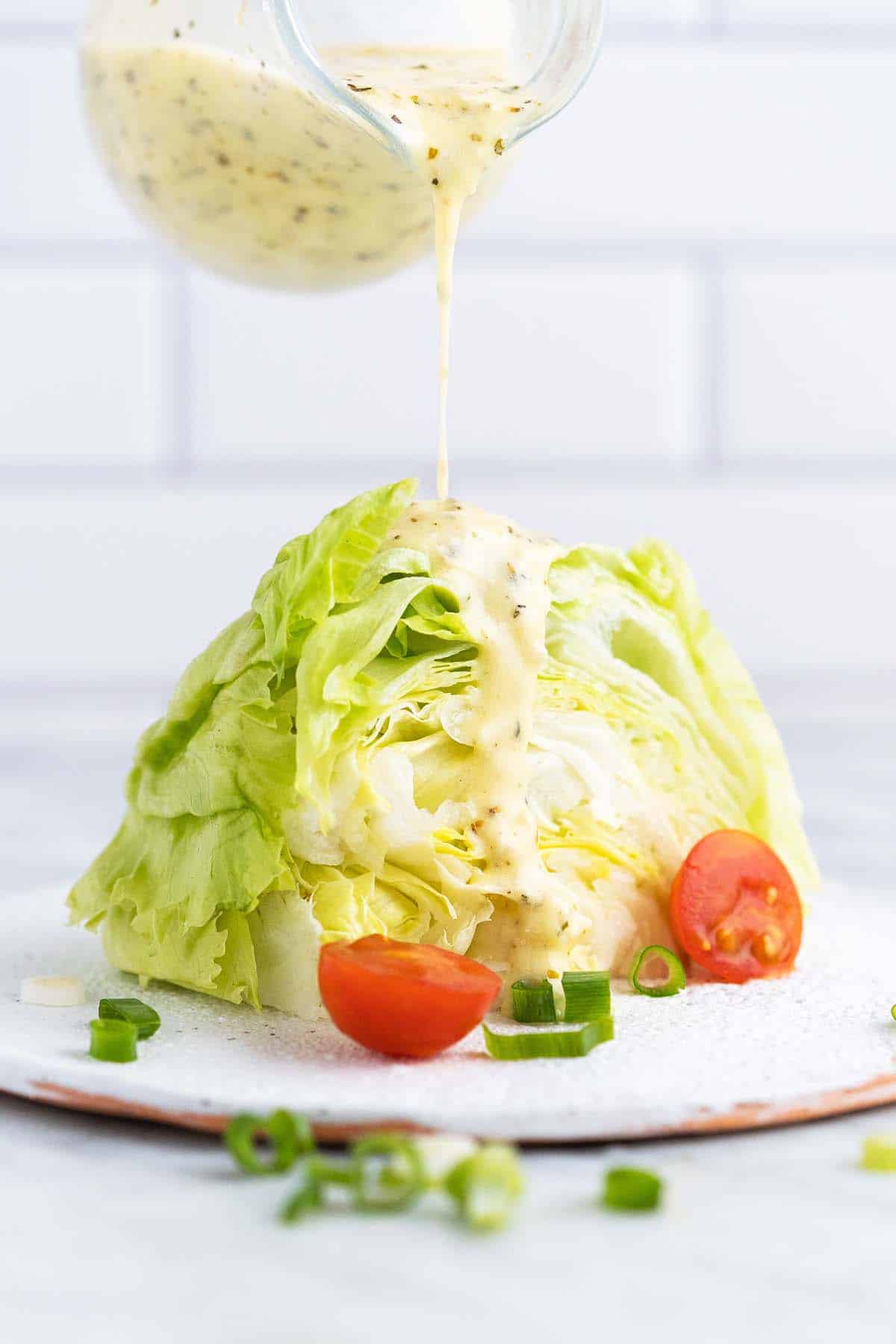 pouring creamy italian dressing on wedge of iceberg lettuce
