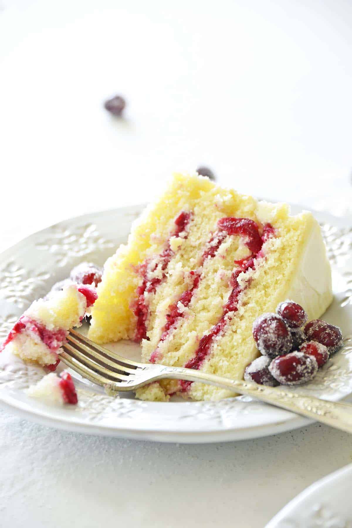 slice of vanilla cake with cranberry filling on individual plate with forkful of cake