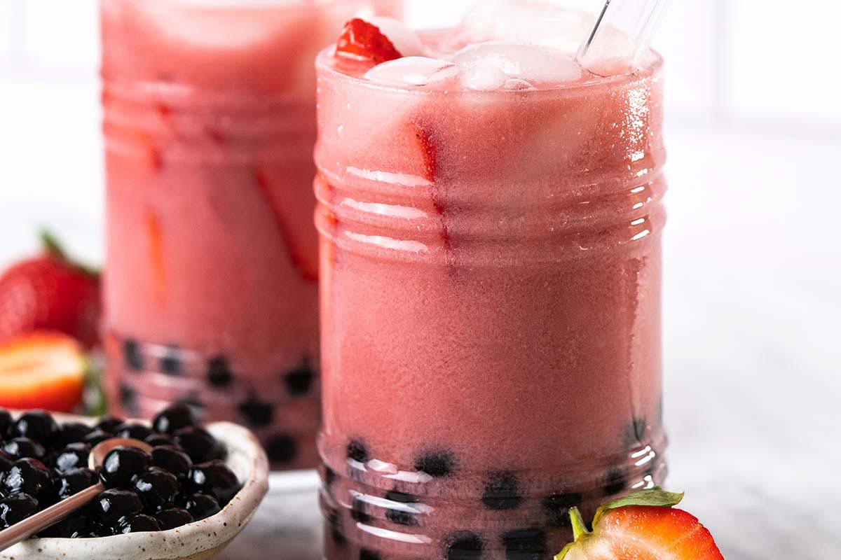 strawberry milk tea in glass next to bowl of boba pearls