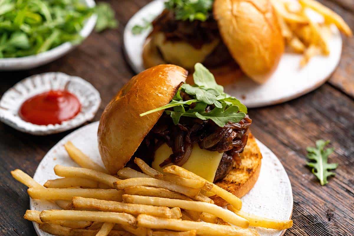 caramelized onion burgers served with french fries on dark wooden table
