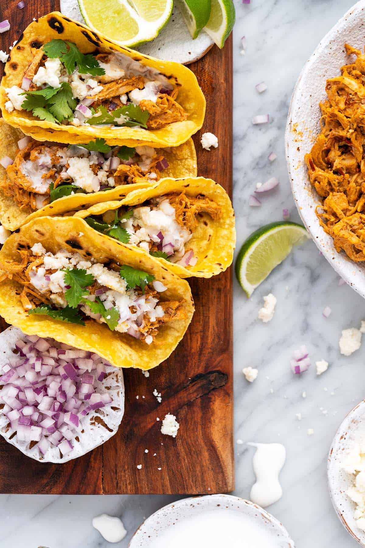 chipotle chicken tacos in corn tortilla shells lined up on wooden plate on marble countertop