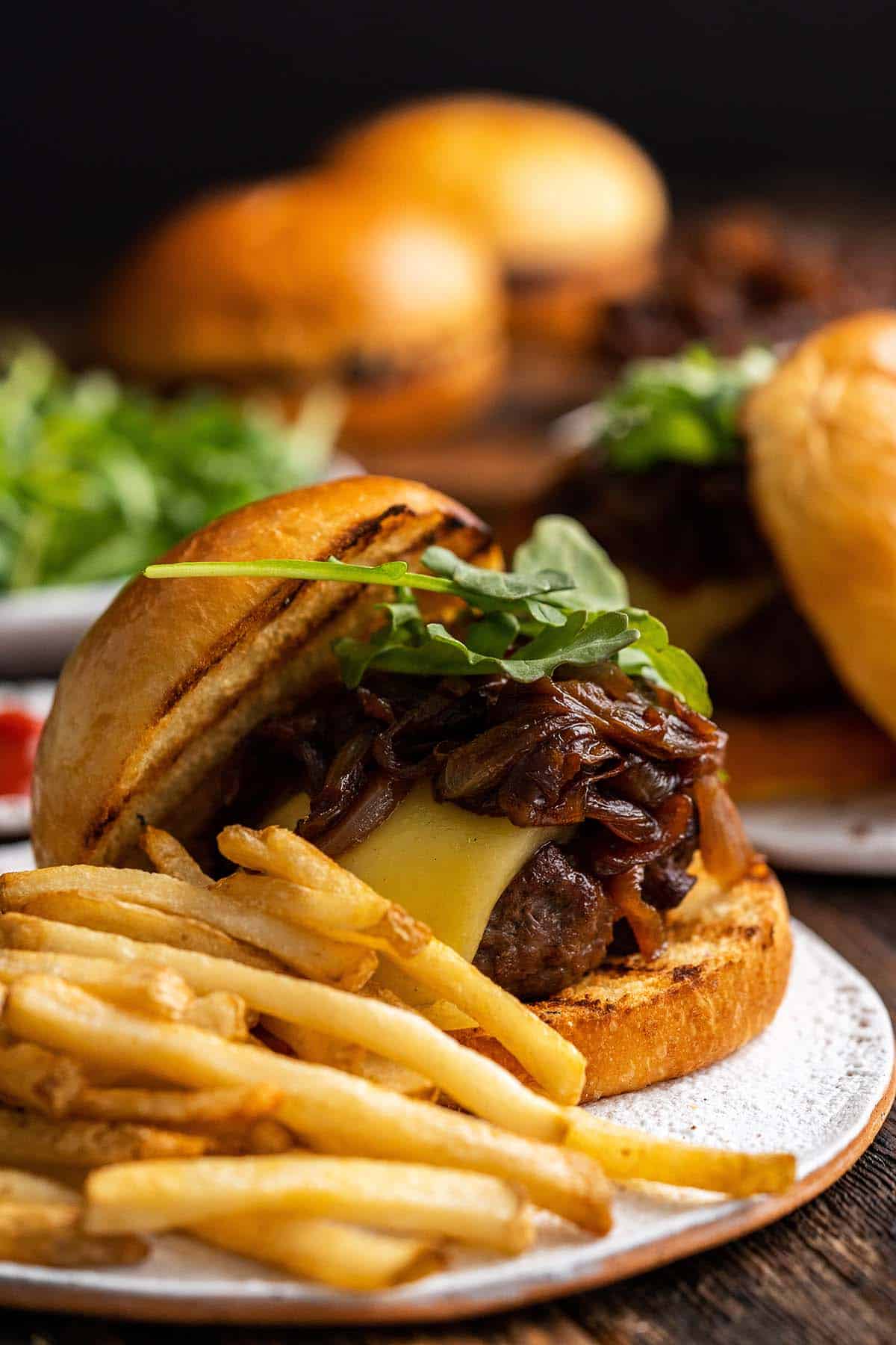 close up front view of caramelized onion burger with fries on white plate