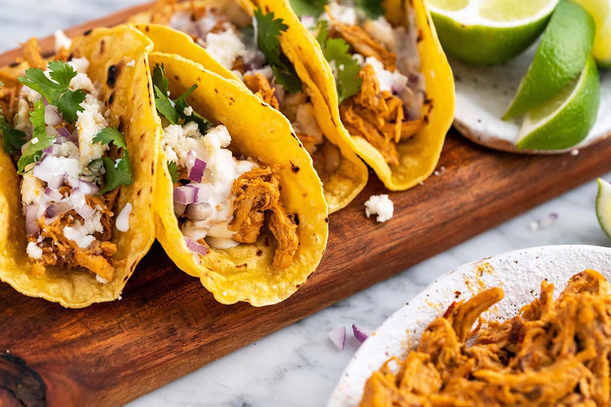 front view of shredded chicken tacos on wooden serving platter