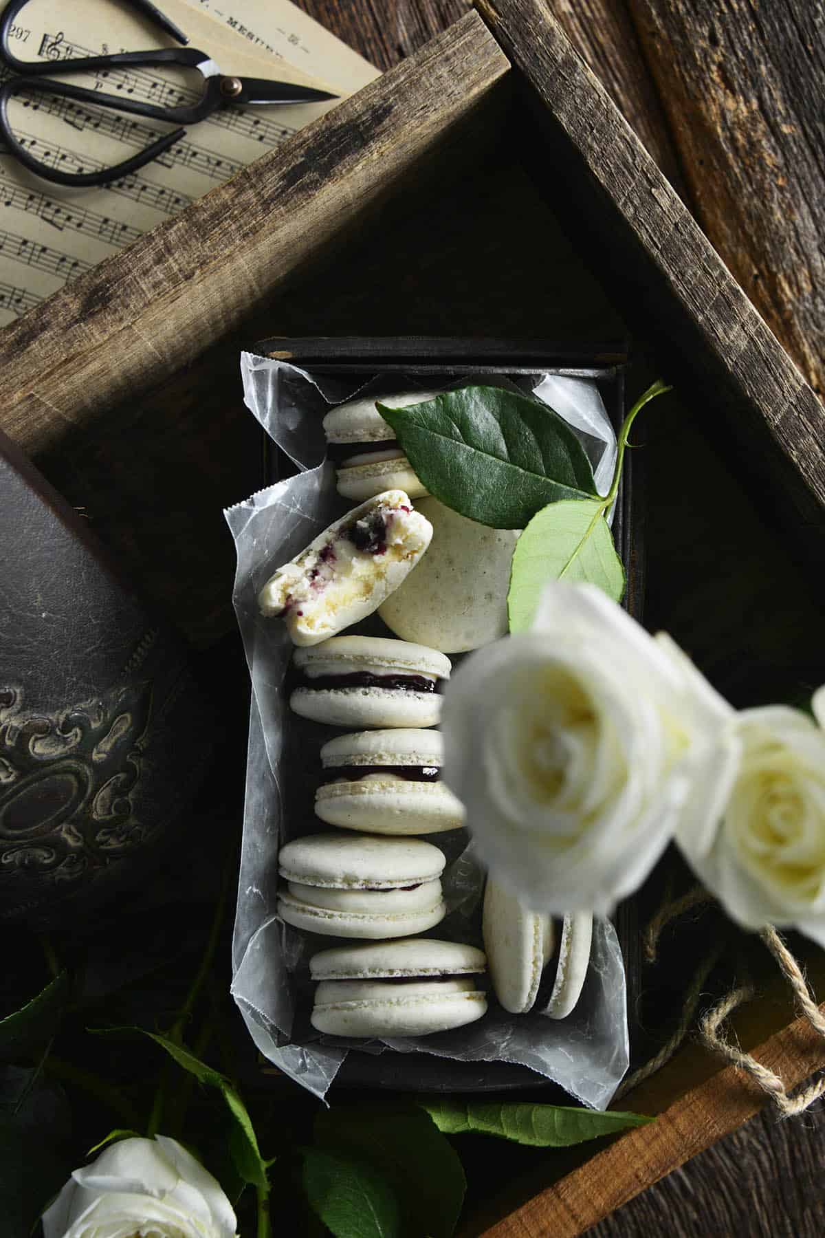 overhead photo of vanilla macarons with blueberry filling with dark and moody styling on wooden board