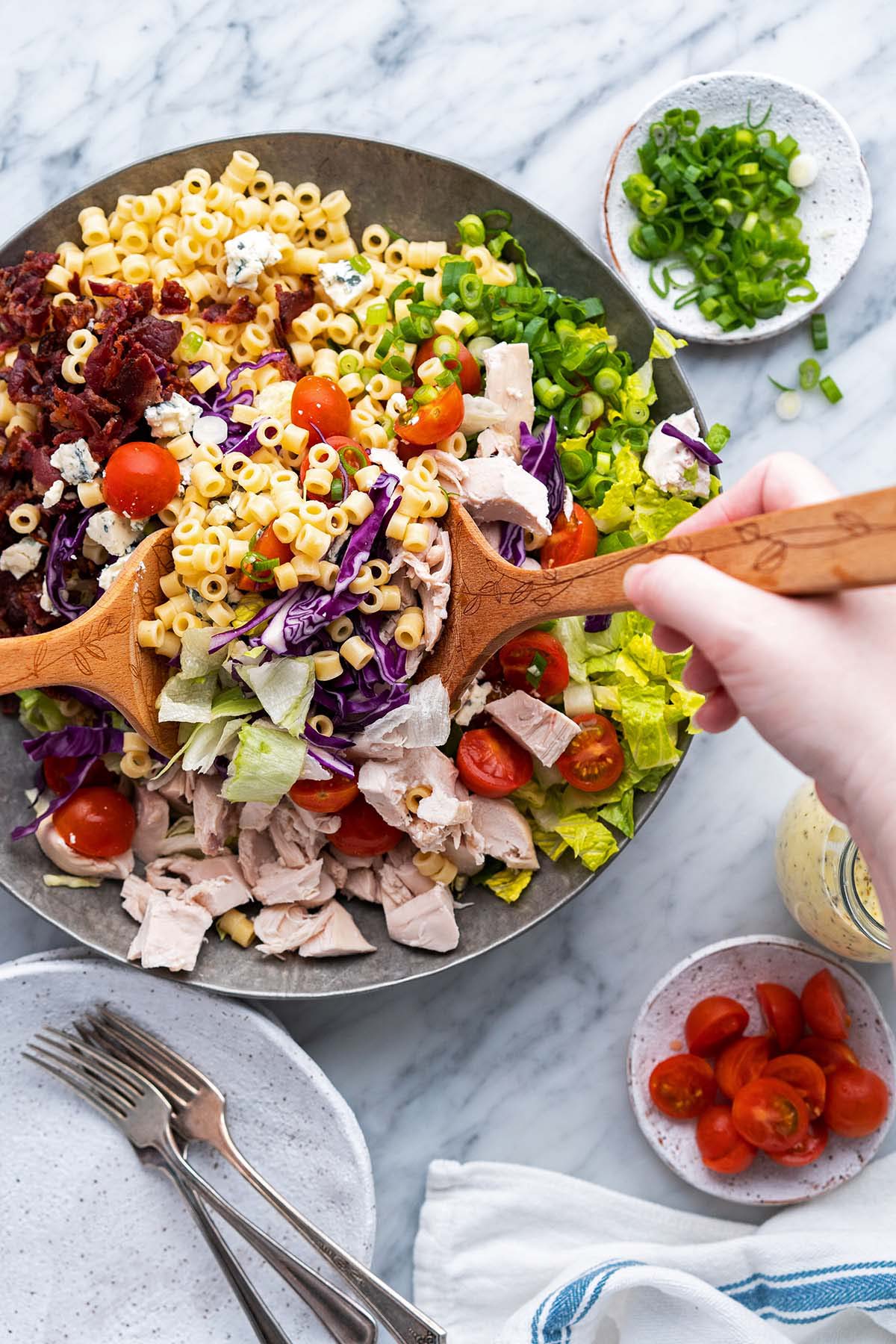 tossing chopped pasta salad with wooden salad spoons