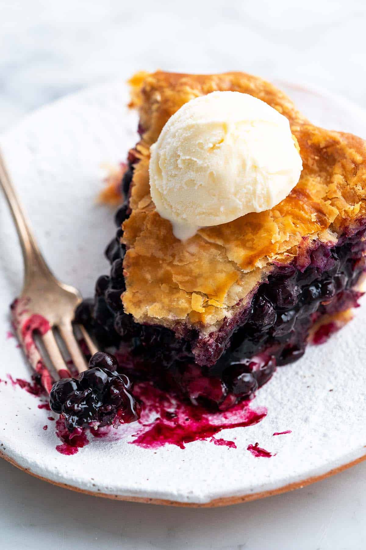 close up of slice of blueberry pie recipe made with frozen blueberries and topped with a scoop of vanilla ice cream