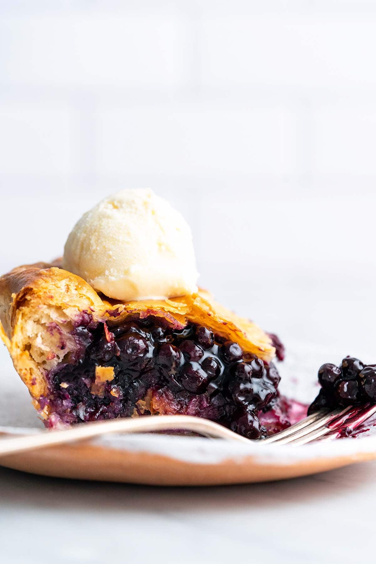 front view of slice of blueberry pie with frozen blueberries topped with vanilla ice cream